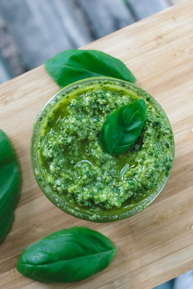 A jar of hemp seed pesto surrounded by fresh basil leaves.