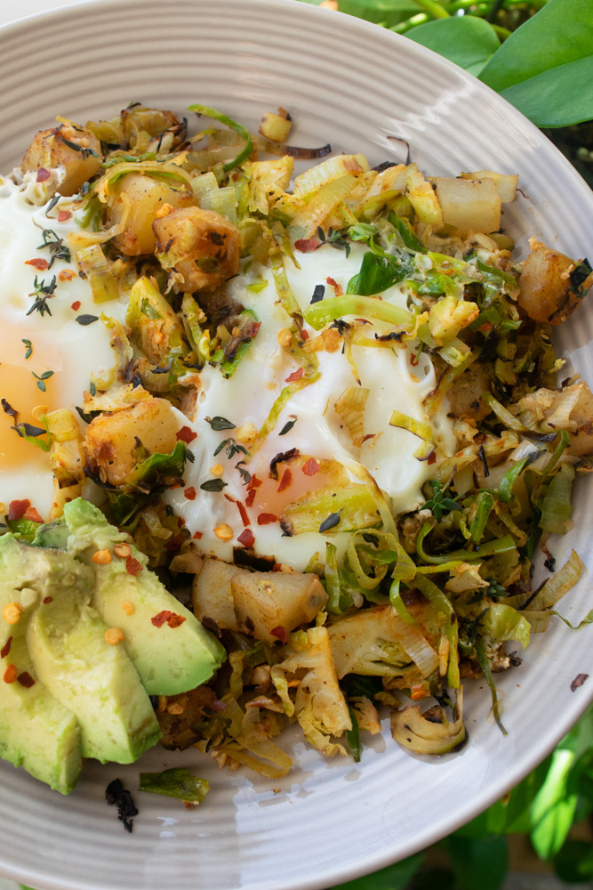 A plate of Brussel sprout and potato hash with eggs and fresh avocado.