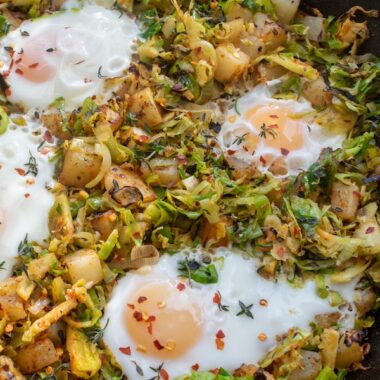 A cast iron skillet filled with a Brussels sprout and potato hash topped with cooked eggs.