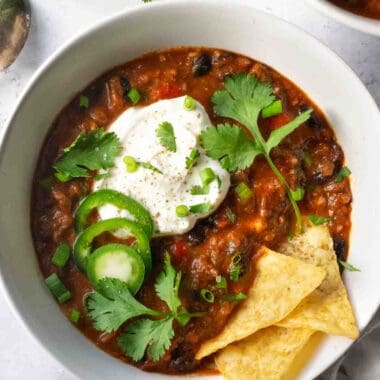 chili in a white bowl topped with yogurt, jalapeno and cilantro.