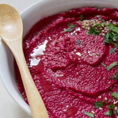 a bowl filled with vibrant roasted beet hummus with a wooden spoon.