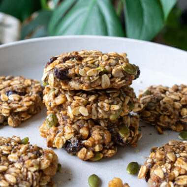 a plate of stacked trail mix cookies in front of a green plant.