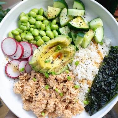 a bowl with spicy salmon, rice, radish, edamame, cucumber and seaweed.