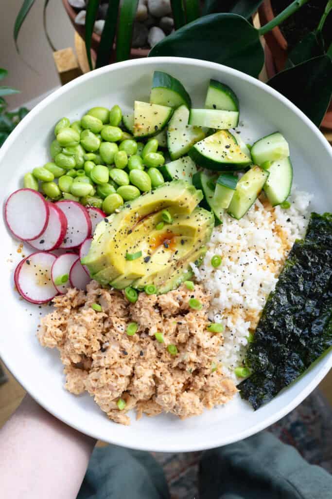 a bowl with spicy salmon, rice, radish, edamame, cucumber and seaweed.