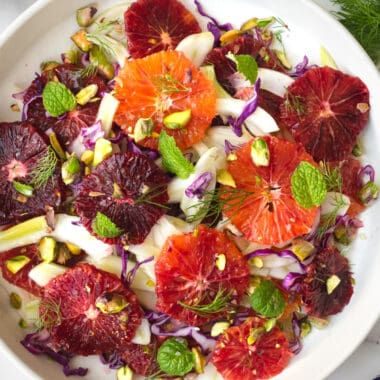 a white plate with a layered blood orange and fennel salad garnished with pistachios, mint and fennel fronds.