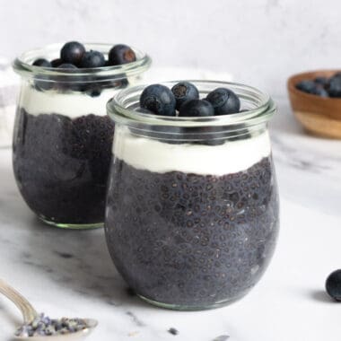 jars of lavender blueberry chia pudding topped with yogurt and blueberries.