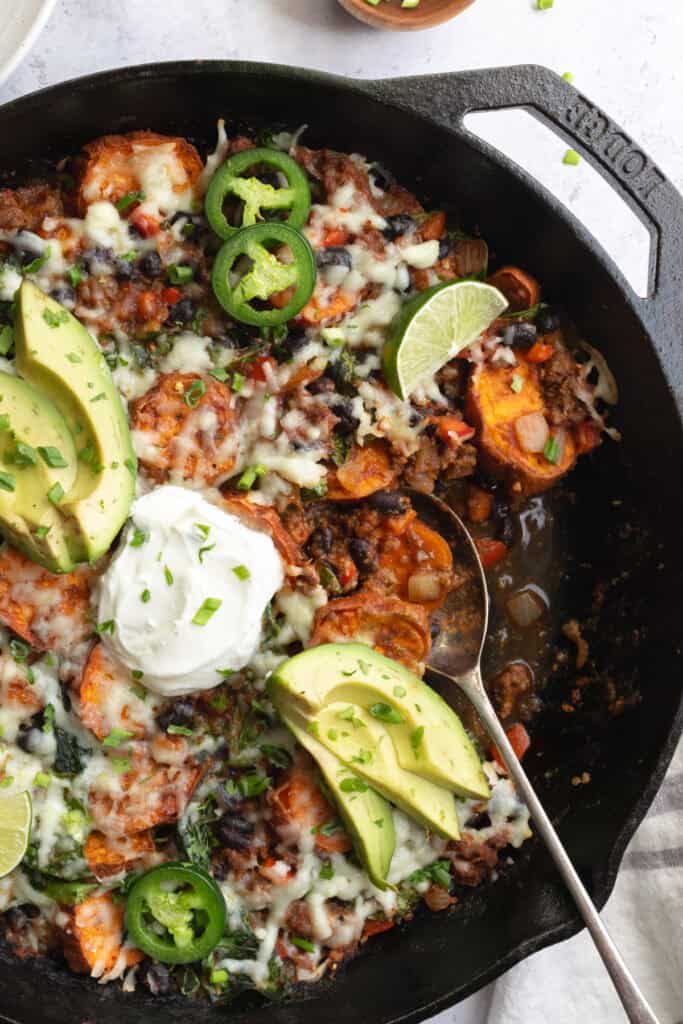 beef and sweet potato taco skillet topped with yogurt, avocado slices and jalapeño slices.