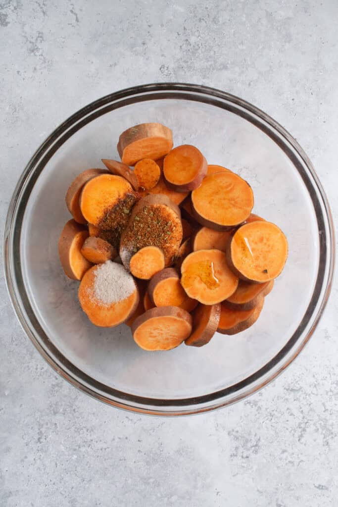 a bowl of sweet potato slices with oil and spices.