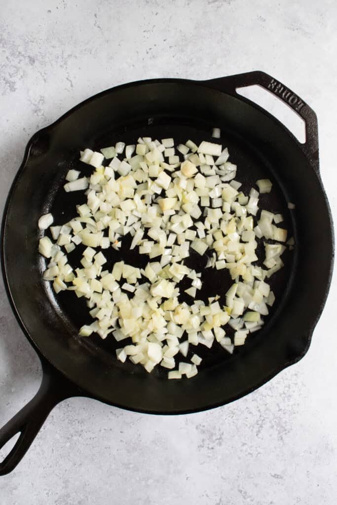 onions being sautéed in a cast iron skillet.