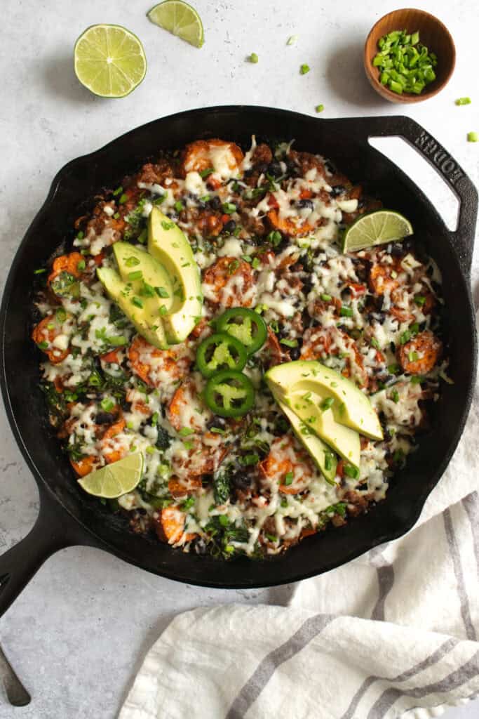beef and sweet potato taco skillet topped with avocado, jalapeño and lime.