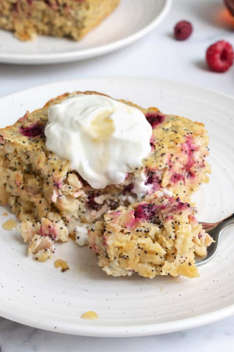 a slice of lemon raspberry baked oatmeal topped with greek yogurt on a white plate.