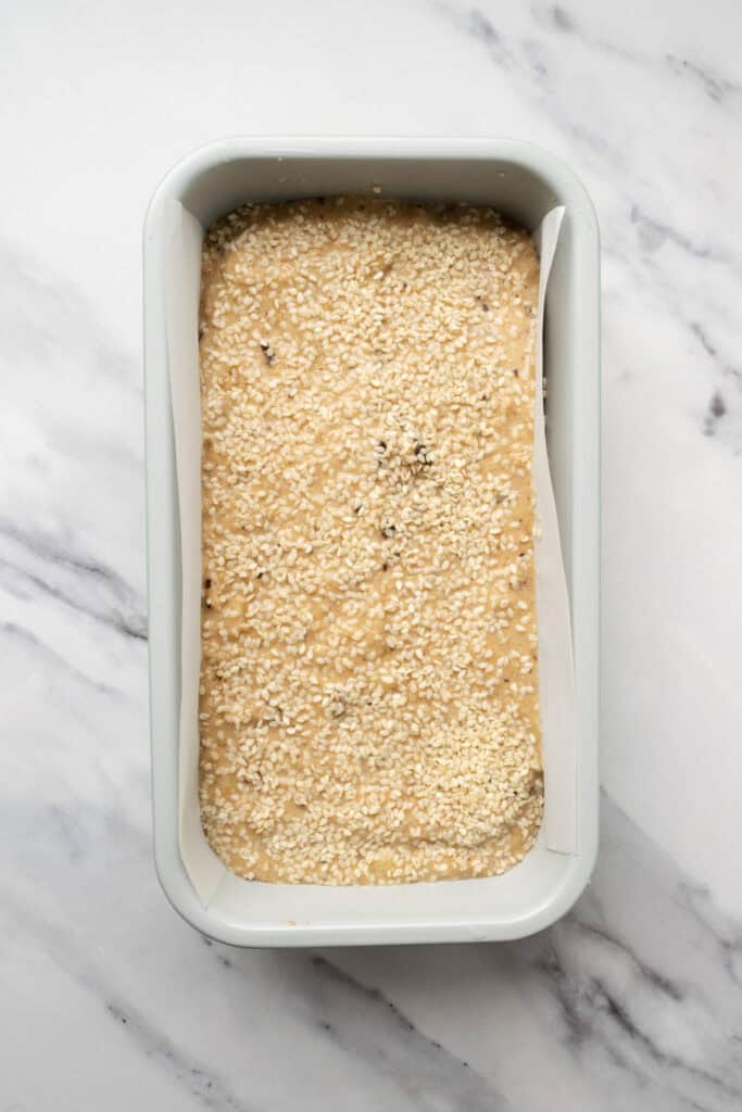 unbaked tahini banana bread topped with sesame seeds in a loaf pan.