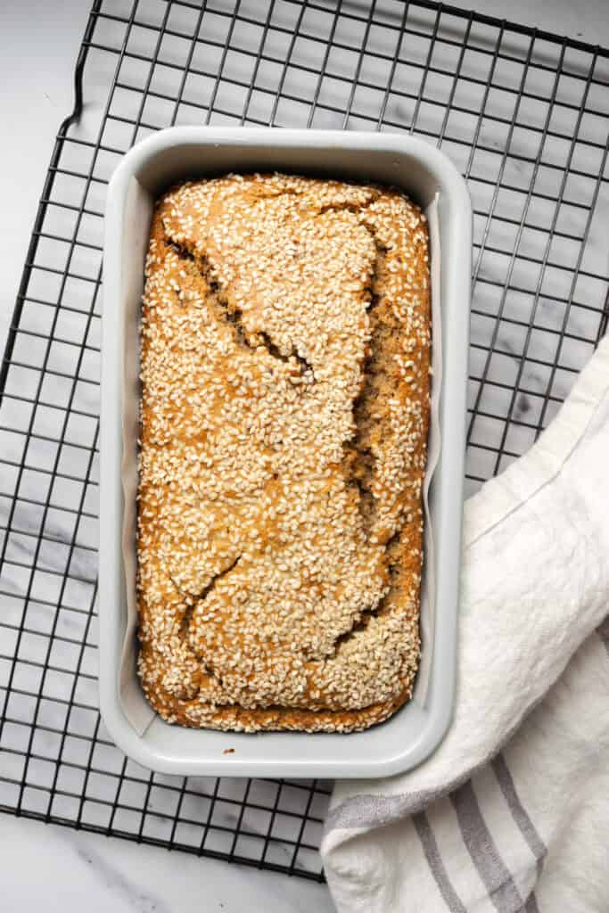 baked tahini banana bread in a loaf pan on a cooling rack.