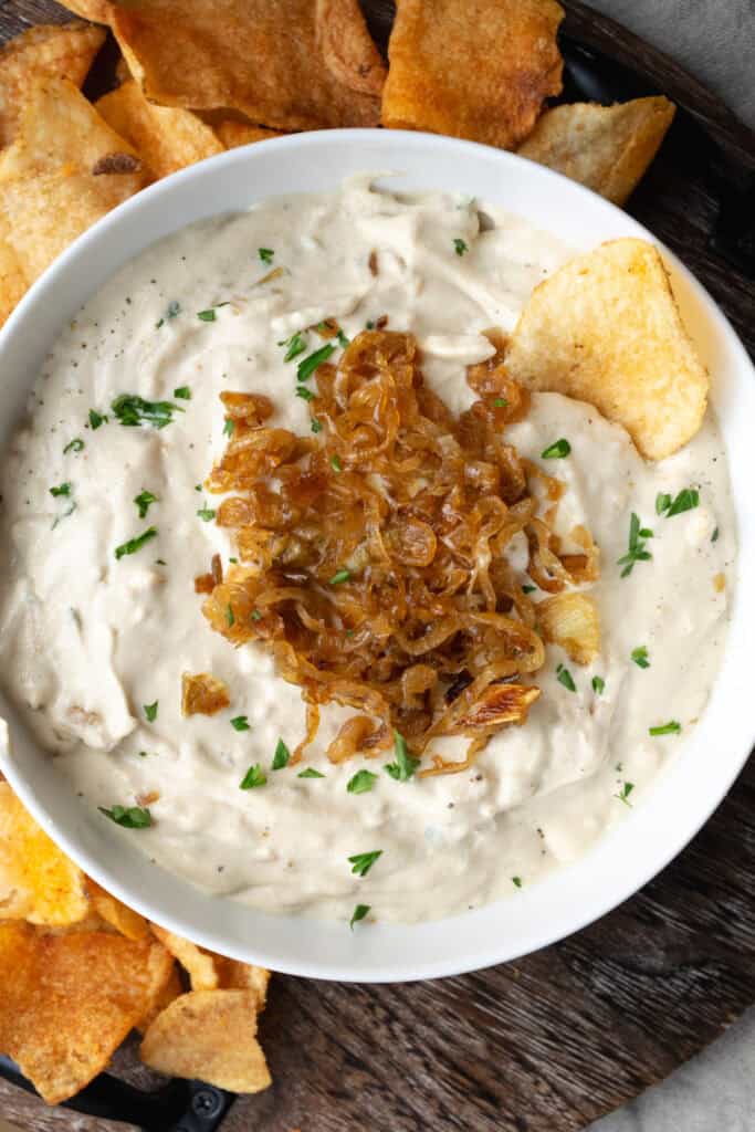 a bowl of vegan French onion dip topped with caramelized onions on a wooden platter with chips.
