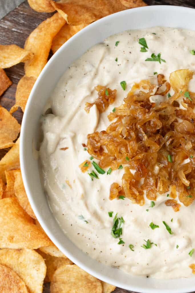 a bowl of vegan French onion dip topped with caramelized onions on a wooden platter with chips.