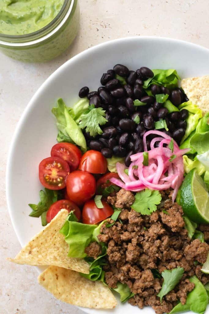 beef taco salad in a white bowl with tortilla chips.