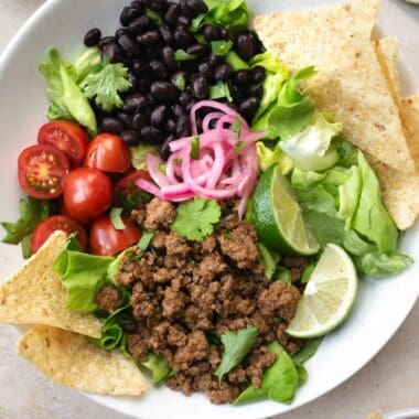 beef taco salad in a white bowl with tortilla chips.