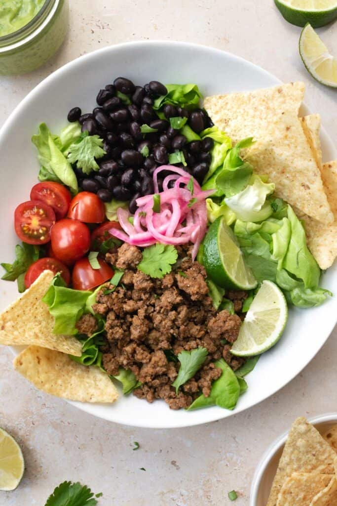 beef taco salad in a white bowl with tortilla chips.