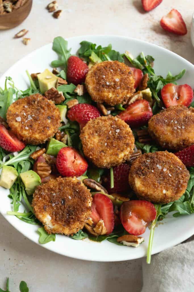 fried goat cheese and strawberry salad in a white bowl.