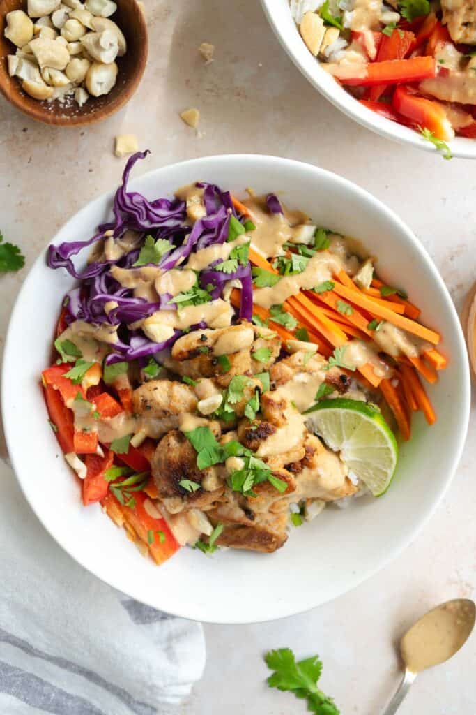 miso peanut chicken bowls with a bowl of chopped cashews and a spoon with miso peanut sauce.