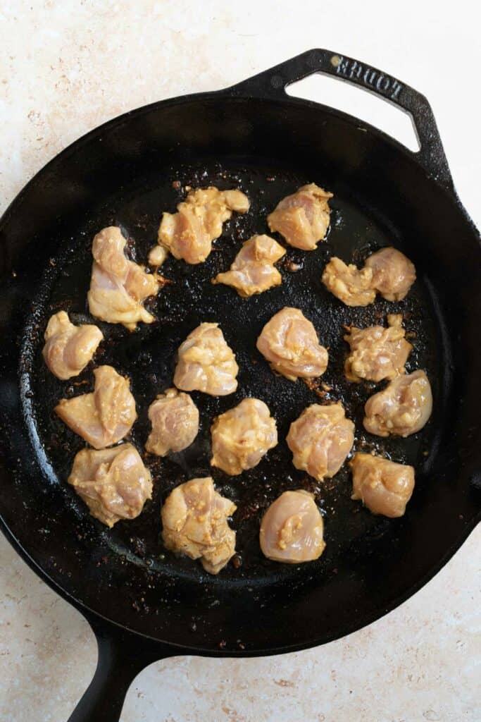 pieces of chicken being cooked in a cast iron skillet.