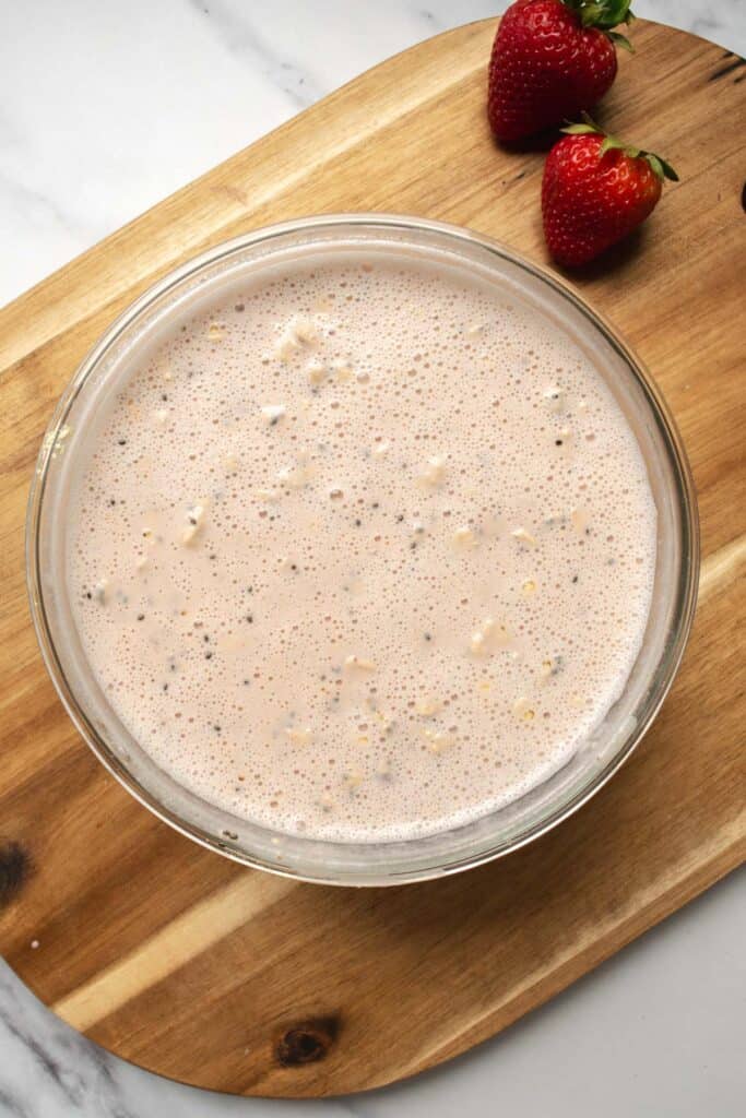 a glass bowl with strawberry milk poured over the oats, protein powder and chia seeds.