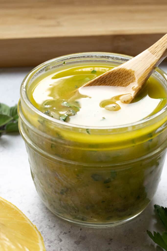 lemon herb vinaigrette in a glass jar with a wooden spoon.