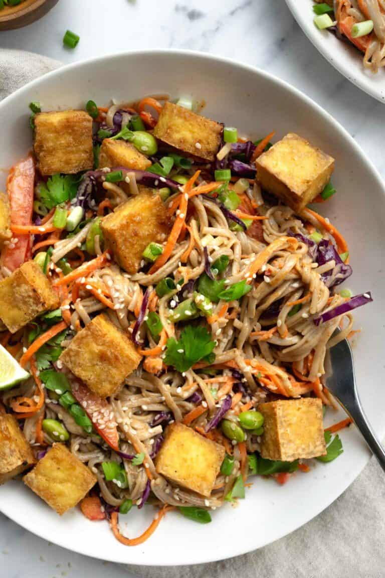 cold soba noodle salad topped with baked tofu in a white bowl.