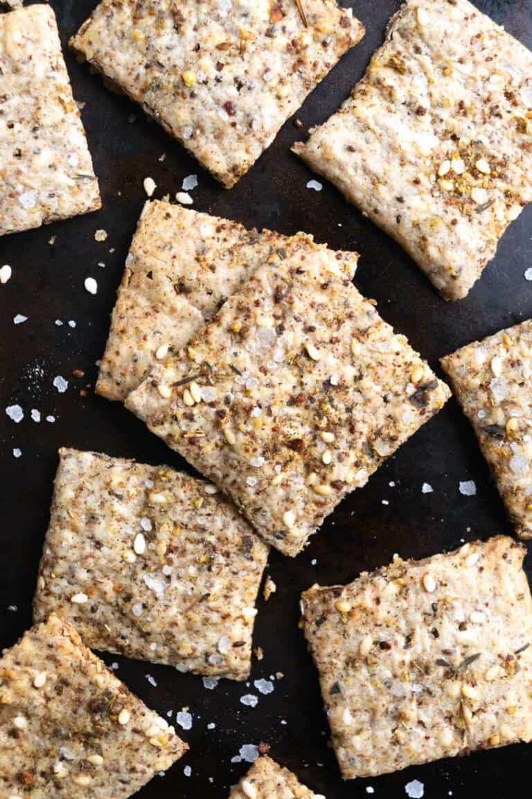 za'atar sourdough discard crackers on a black baking sheet with flaked sea salt.