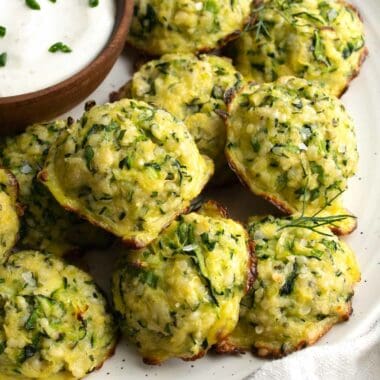 zucchini bites on a white plate with a small wooden bowl filled with ranch dressing.