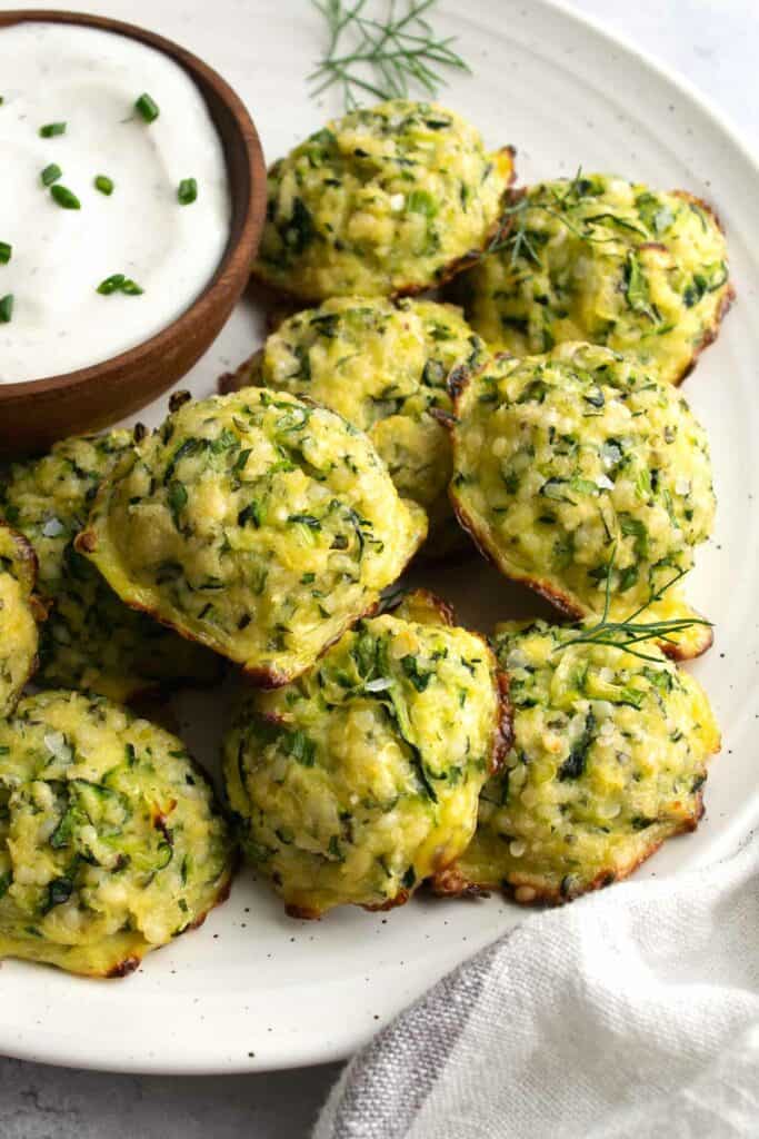 zucchini bites on a white plate with a small wooden bowl filled with ranch dressing.