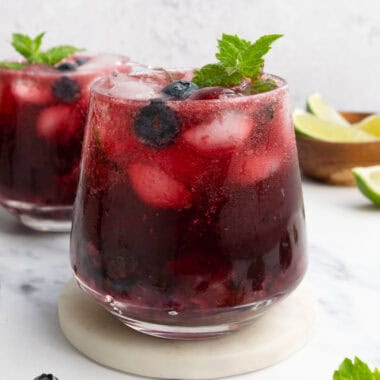 two glasses of hibiscus blueberry mocktails topped with fresh mint and blueberries.