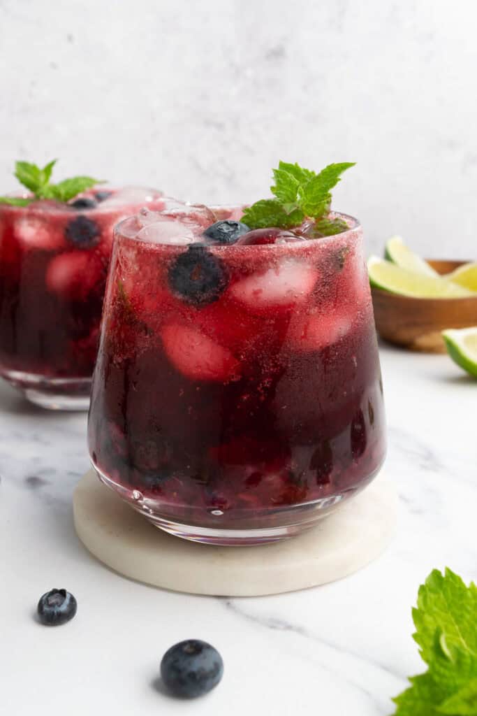 two glasses of hibiscus blueberry mocktails topped with fresh mint and blueberries.