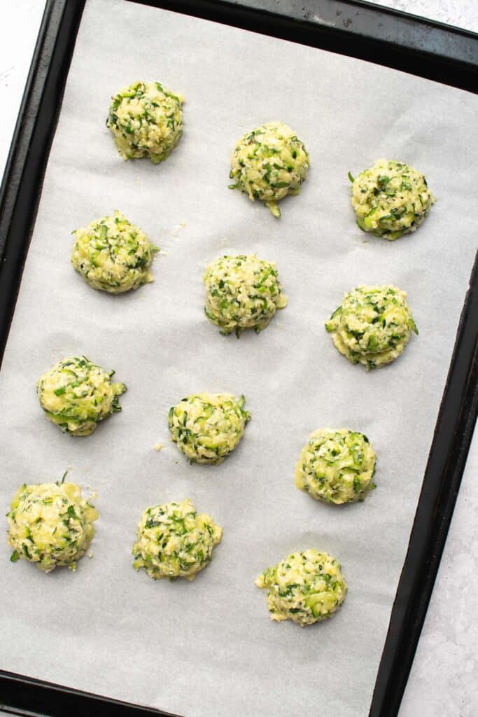 zucchini mixture shaped into balls on a baking sheet lined with parchment paper.