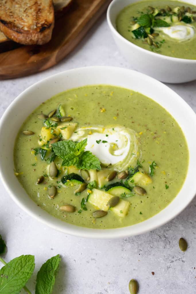 two bowls of zucchini leek soup with a cutting board and toasted bread.