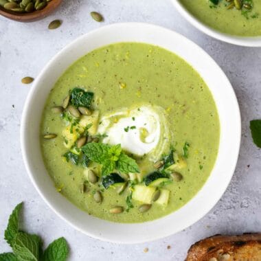 two bowls of zucchini leek soup, a small bowl of pumpkin seeds, toasted bread and a sprig of fresh mint.