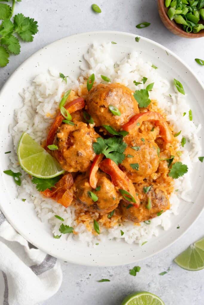 a white plate topped with white rice, turkey meatballs and red curry sauce.