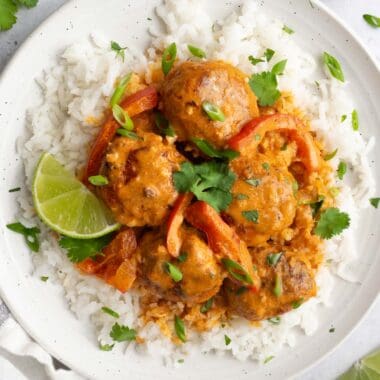 a white plate topped with white rice, turkey meatballs and red curry sauce.