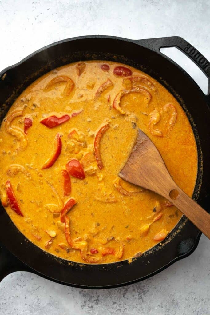 red curry sauce in a skillet with a wooden spoon.