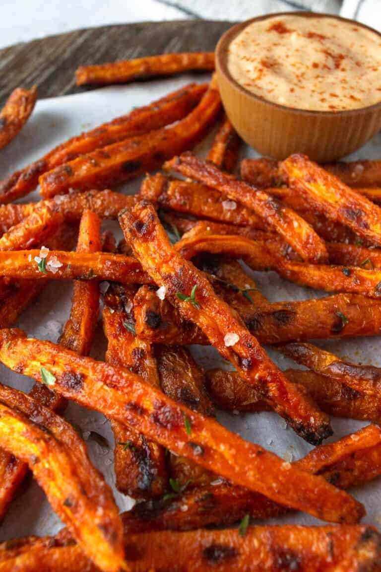 baked carrot fries on parchment paper and a wooden bowl with aioli.