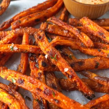 baked carrot fries on parchment paper and a wooden bowl with aioli.