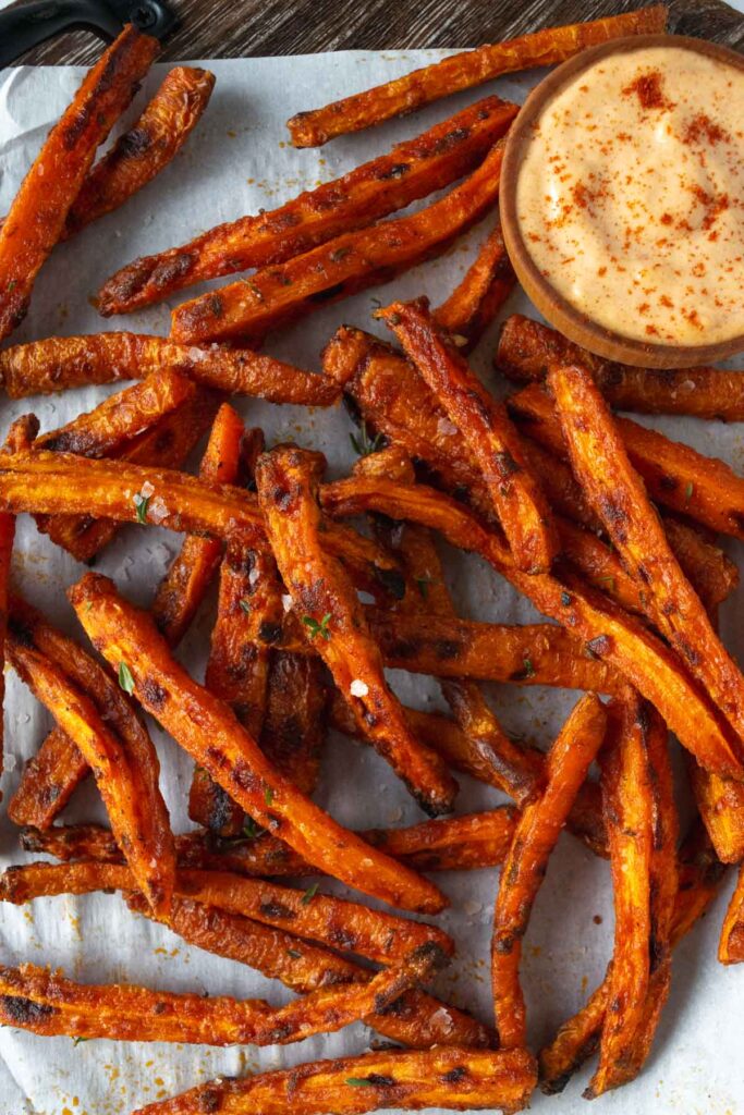 carrots fries on a board with parchment paper and a bowl of aioli.