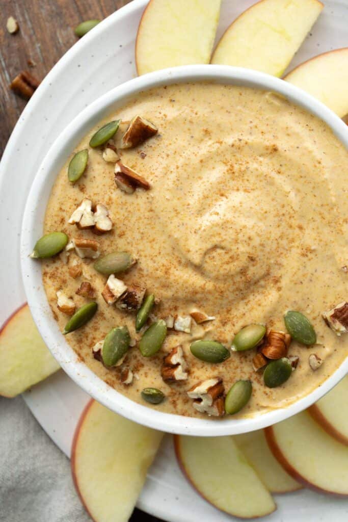 pumpkin fruit dip in a white bowl surrounded by apple slices.