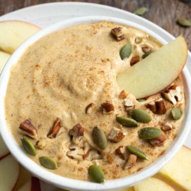 pumpkin fruit dip in a white bowl, topped with pecans and pumpkin seeds.