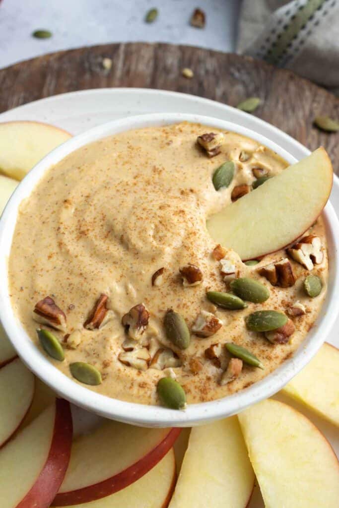 pumpkin fruit dip in a white bowl, topped with pecans and pumpkin seeds.