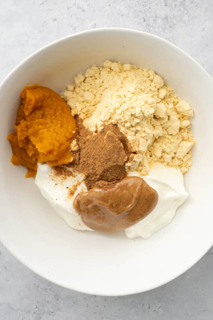 yogurt, pumpkin, protein powder, almond butter and spices in a white bowl.