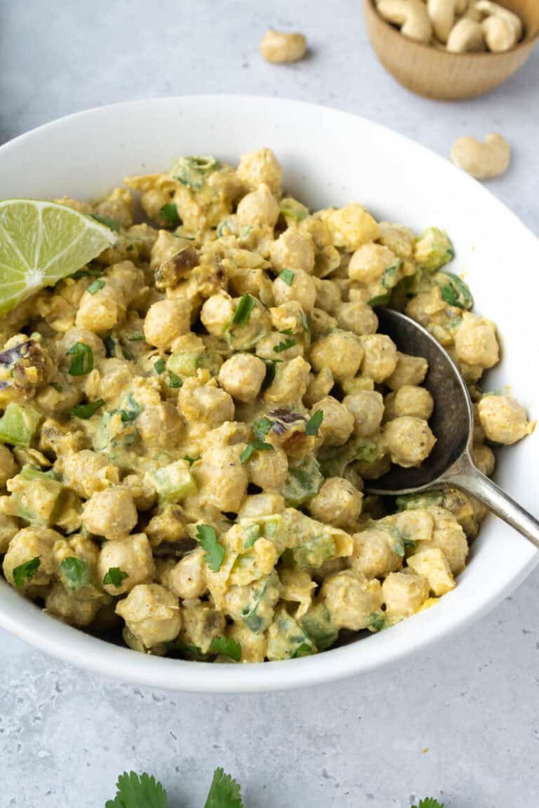 curried chickpea salad in a white bowl with a lime wedge and spoon.