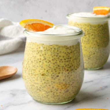 orange creamsicle chia pudding in glass jars topped with yogurt and a small orange slice.