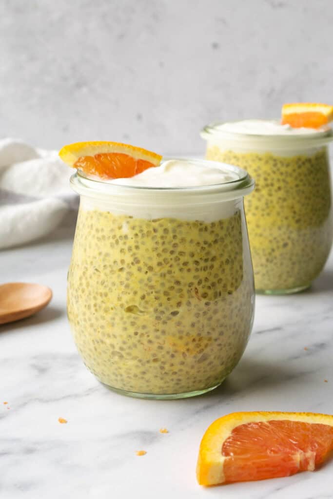 orange creamsicle chia pudding in glass jars topped with yogurt and a small orange slice.