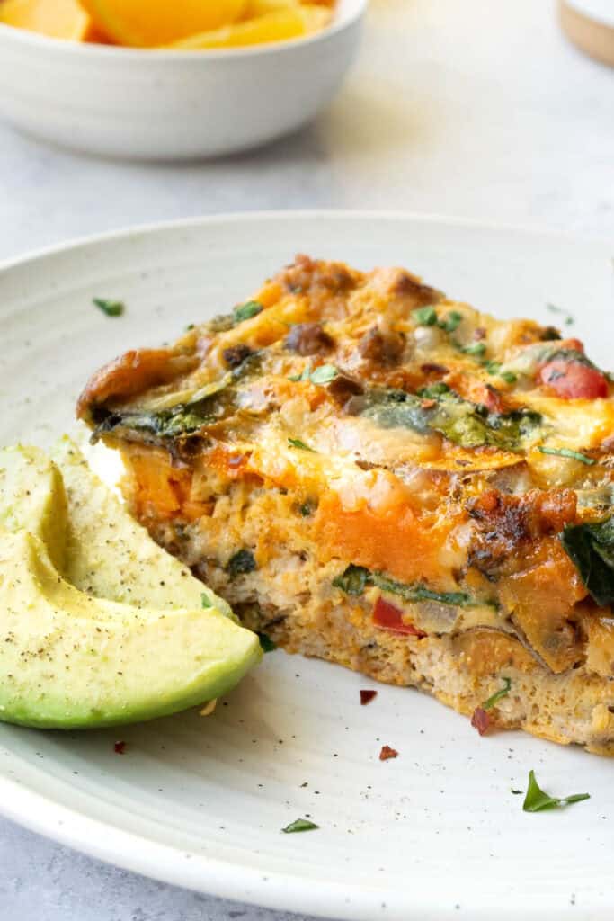 breakfast casserole slice on a white plate with avocado